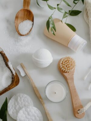 Flat lay of natural spa essentials including salts, soap, brush, and greenery.