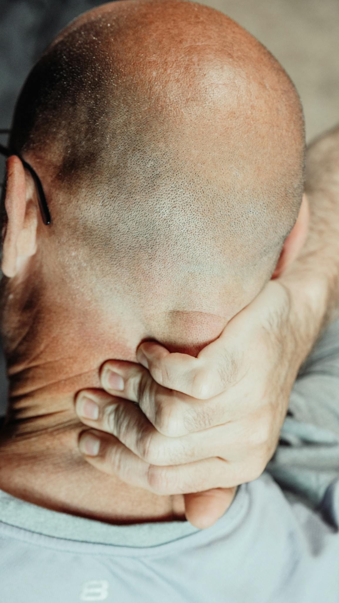 A bald man holding his neck to soothe discomfort, highlighting neck pain relief methods.